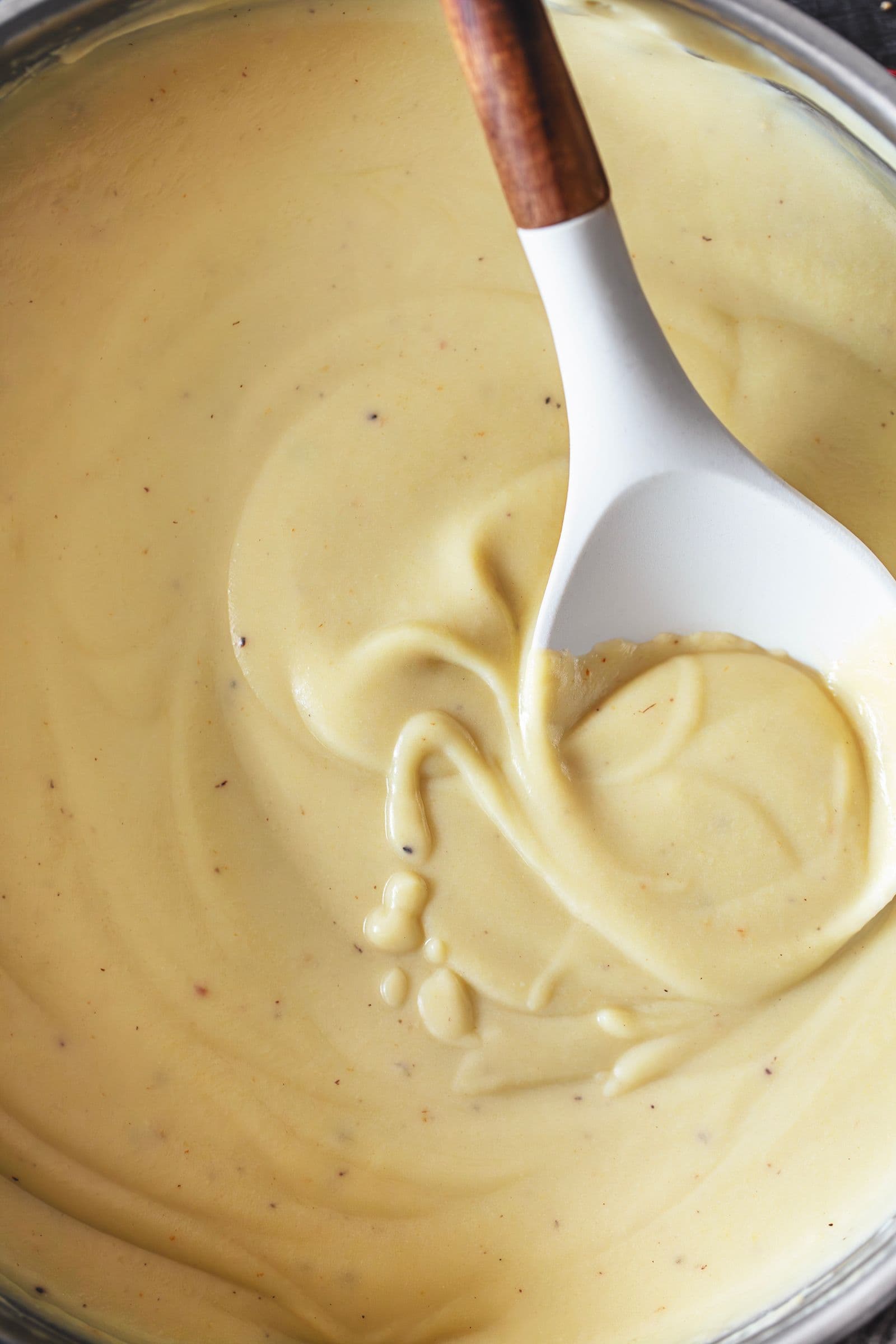 Creamy vegan and gluten-free béchamel sauce in a pot, stirred with a white spoon with a wooden handle