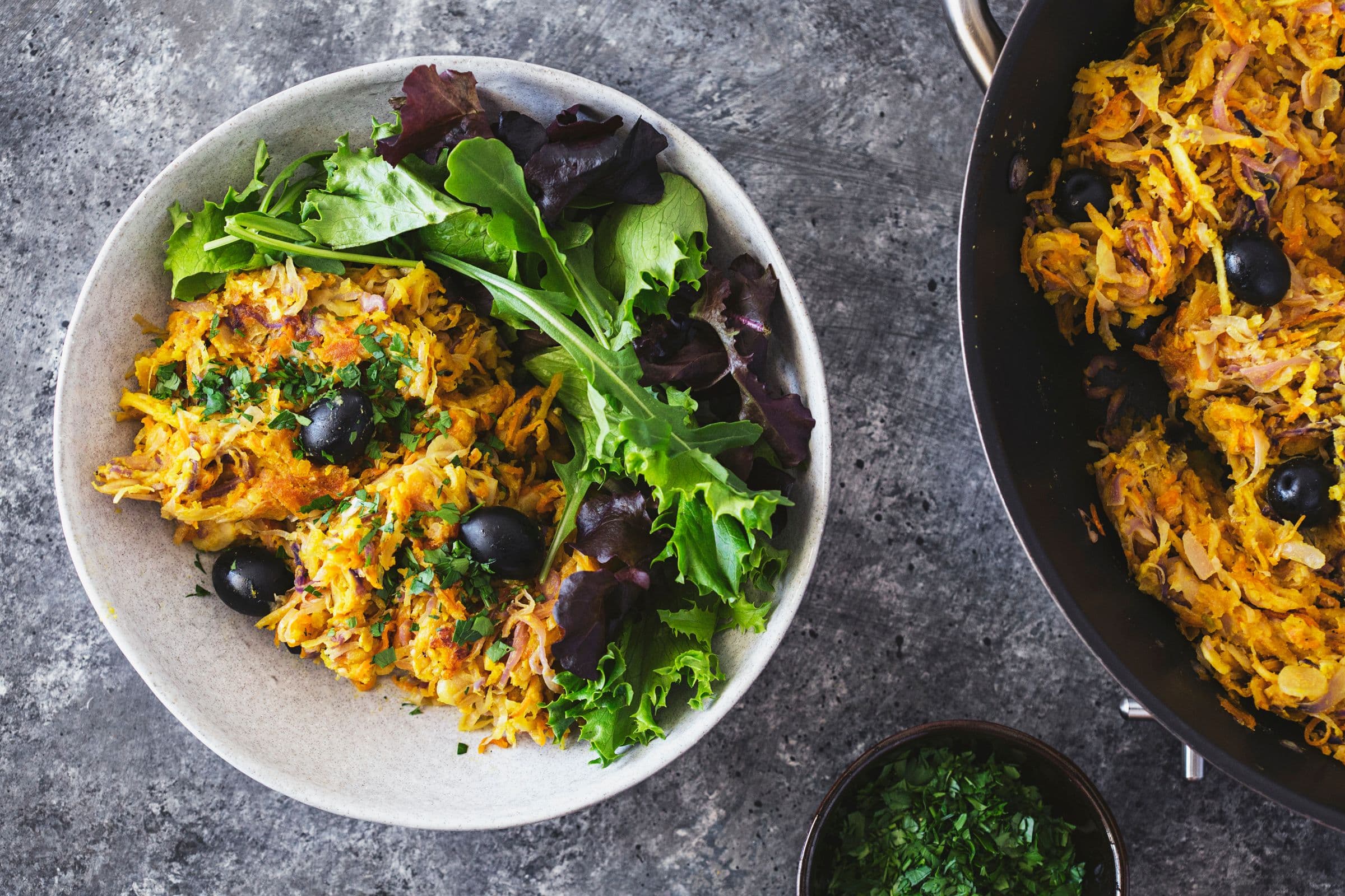 Portuguese veggie hash garnished with black olives and chopped parsley, and plated with fresh green salad on the side.