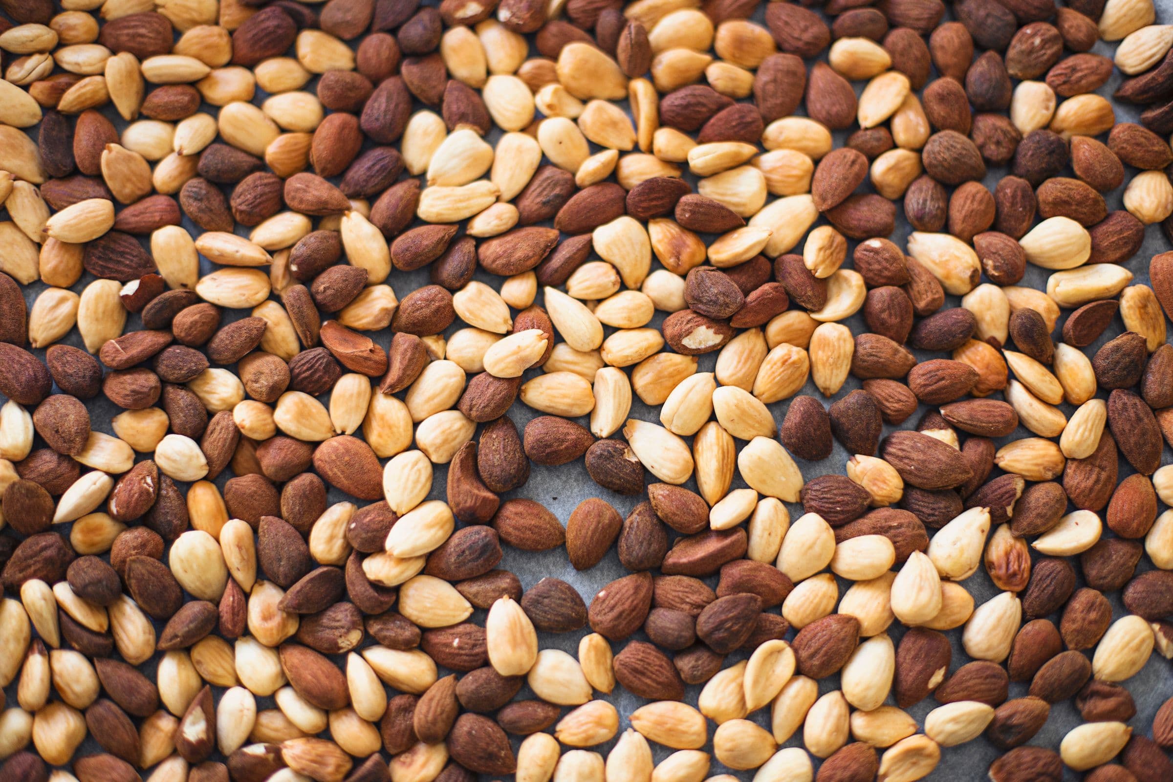 Close-up of raw almonds and peeled almonds spread out on a flat surface.