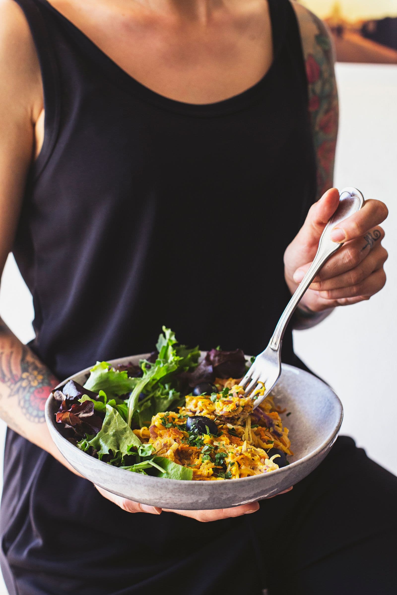 Person holding a bowl of veggie hash with green salad, ready to eat.
