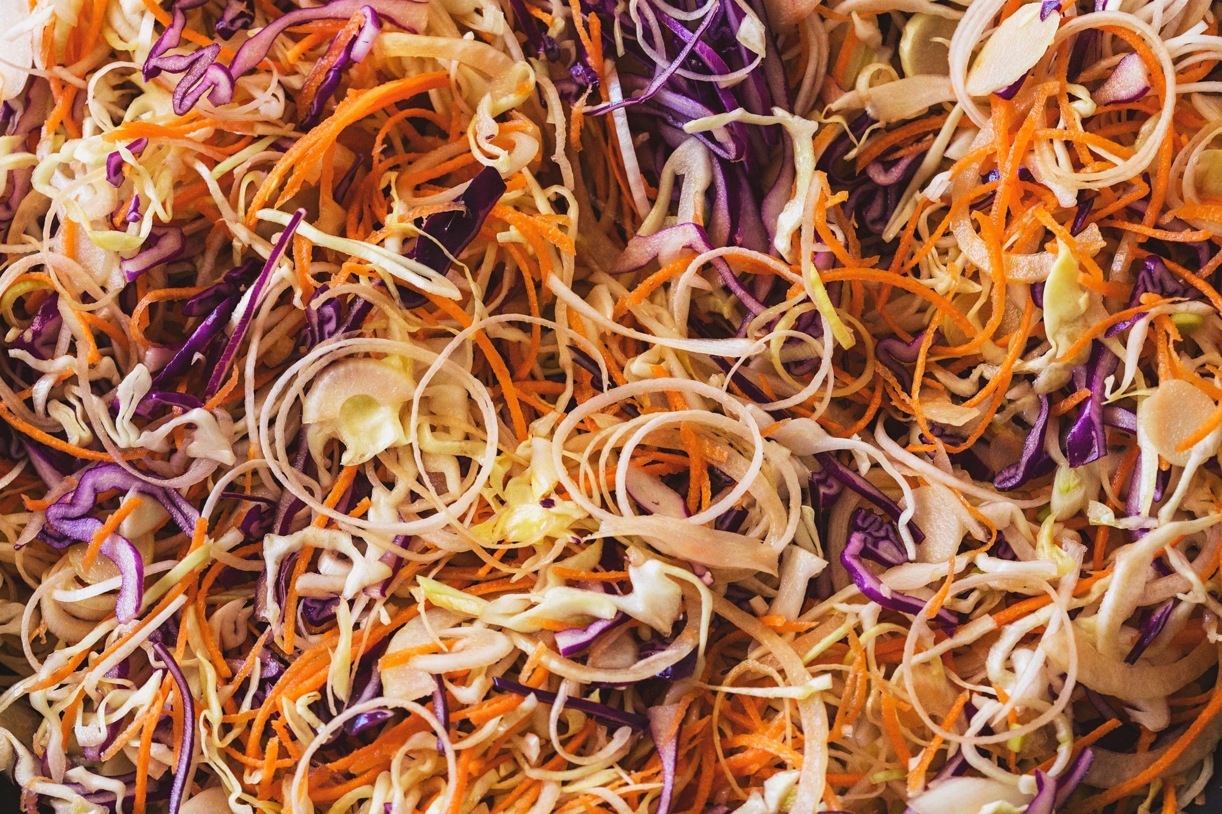 Close-up texture of raw sliced carrots, cabbage, leeks and onions.
